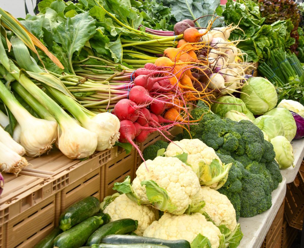 a picture of a vegtable stall at a farmers market displaying various winter vegtables such as carrots, parsnips, cauliflower and broccoli
