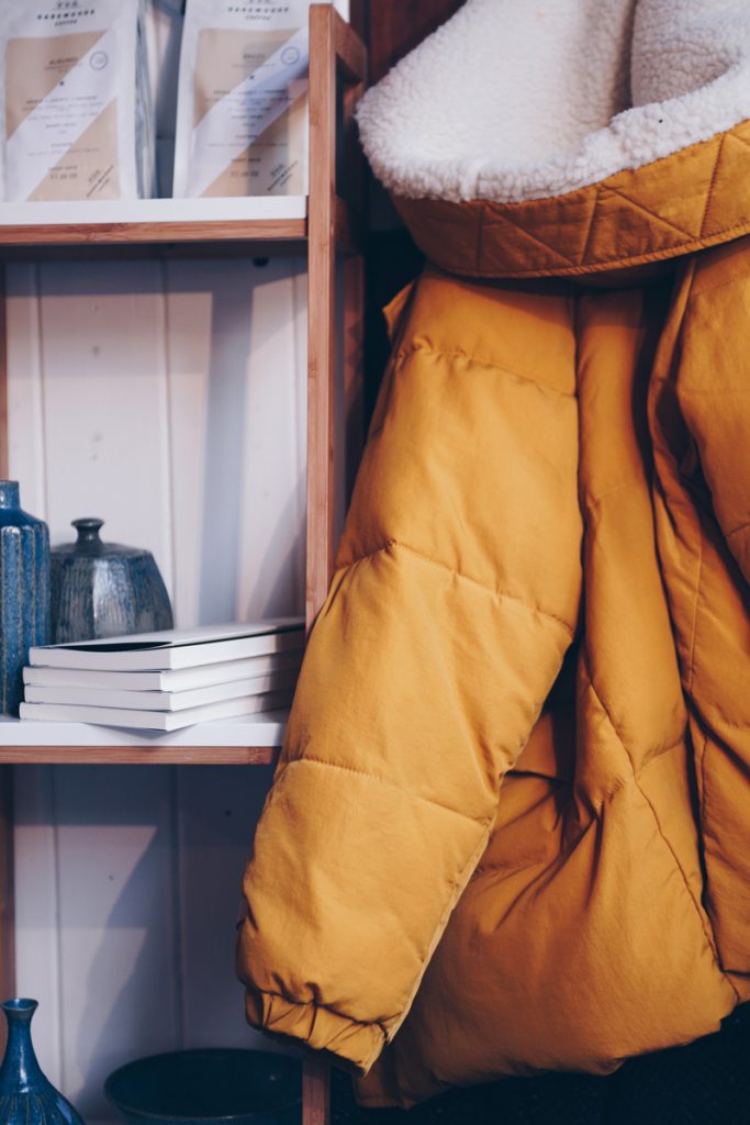a mustard sherpa lined winter coat next to a shelving unit