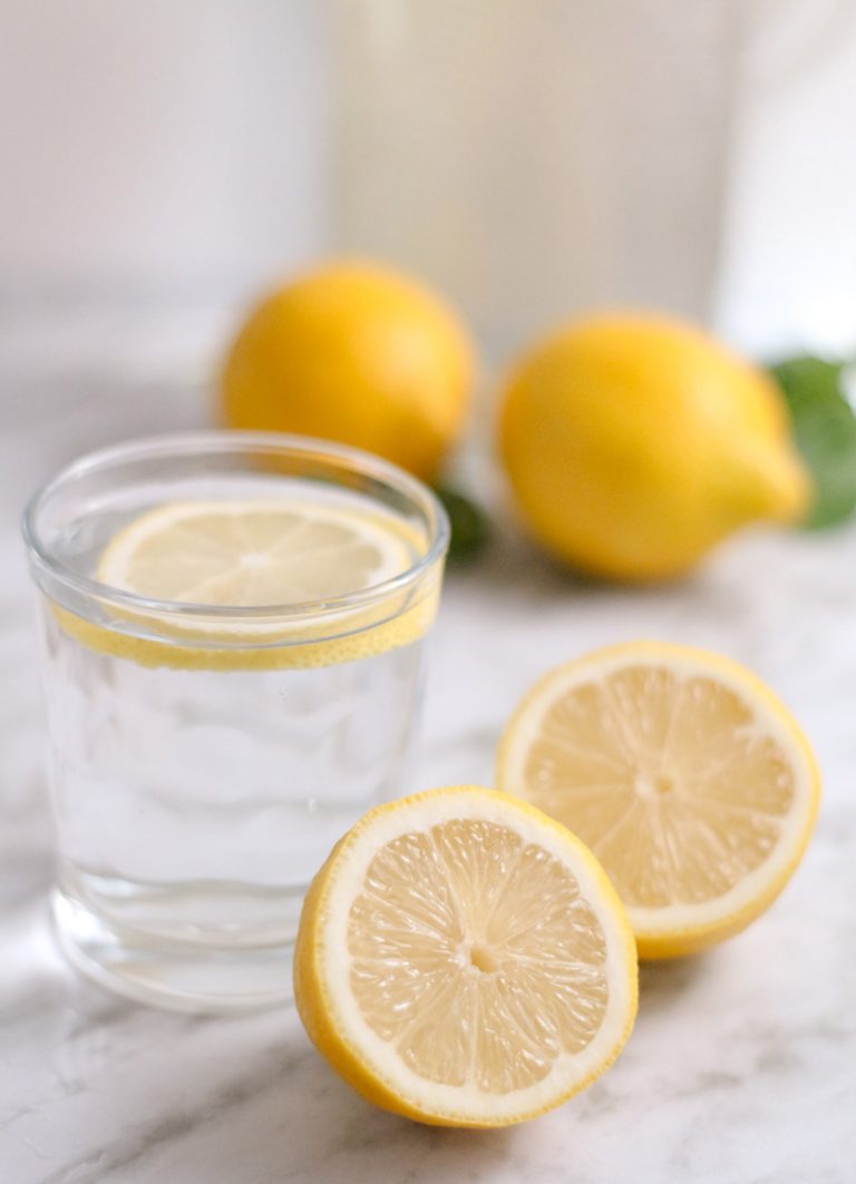 glass of water with a sliced lemon inside and lemons around the glass