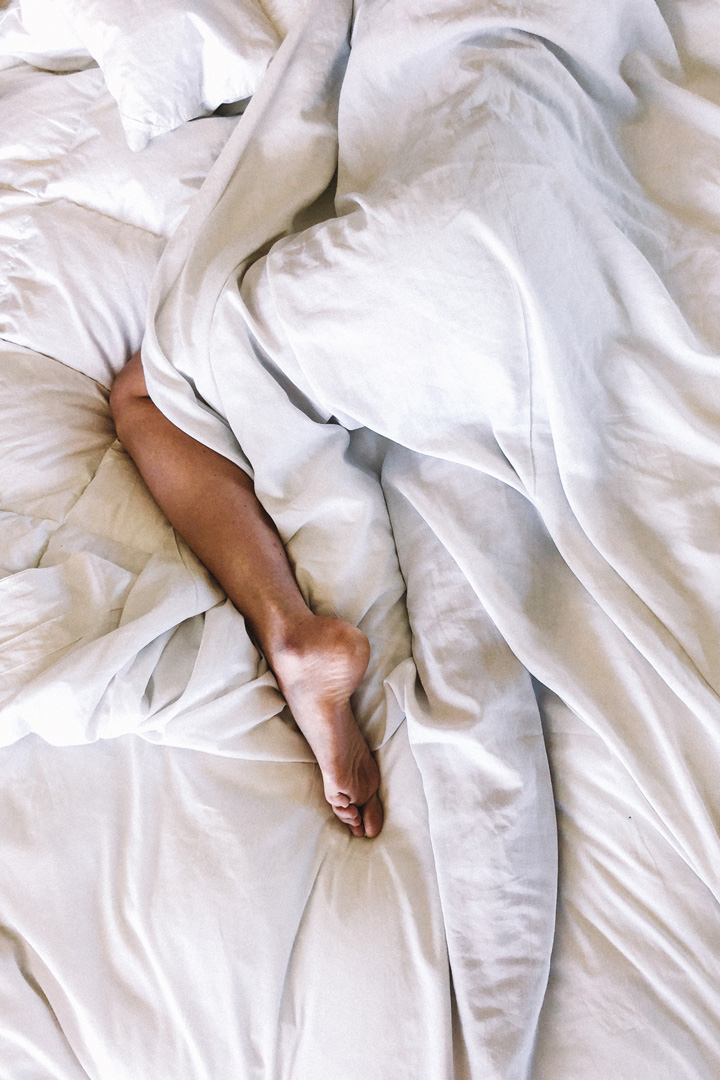 a picture of a leg wrapped around in white bed sheets | health tips for winter don't stay in bed too long