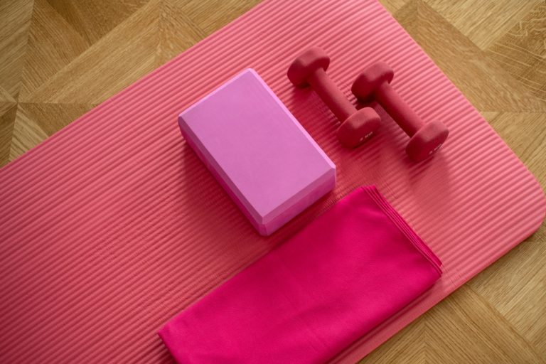 pink exercise mat rolled out on floor with yoga block and weights
